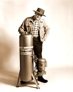 The founder Frank Davey posing with his long cylindrical tube-based water pump seated on a tri-stand. The horsepower and specs of this water pump remains unknown.